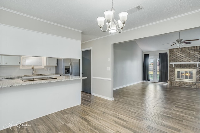 kitchen with white cabinets, open floor plan, hanging light fixtures, a brick fireplace, and stainless steel fridge with ice dispenser