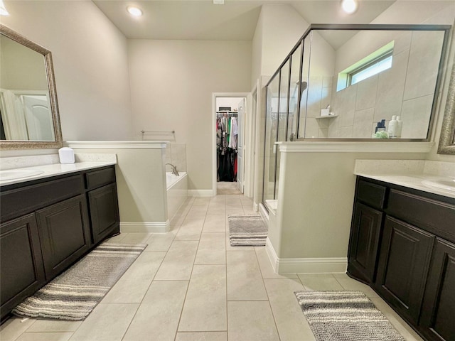 bathroom featuring a garden tub, tile patterned flooring, a spacious closet, a shower stall, and two vanities