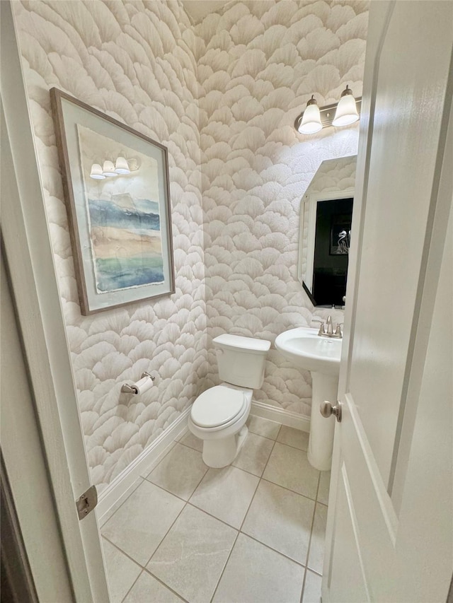 half bathroom with toilet, baseboards, and tile patterned floors