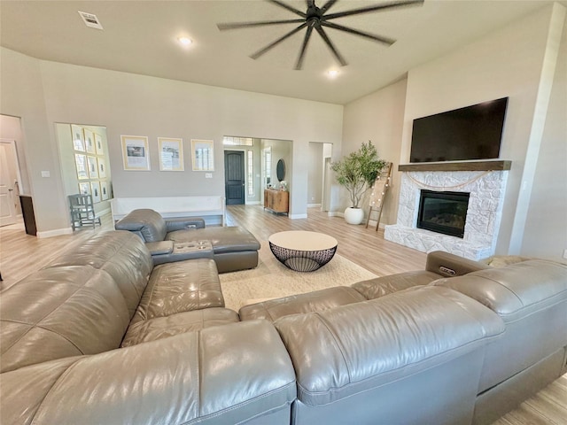 living room with light wood-style floors, visible vents, a stone fireplace, and baseboards