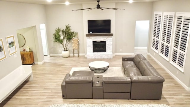 living area with light wood-type flooring, ceiling fan, a premium fireplace, and baseboards