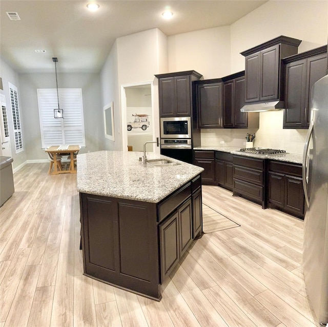 kitchen featuring decorative light fixtures, stainless steel appliances, a sink, an island with sink, and under cabinet range hood