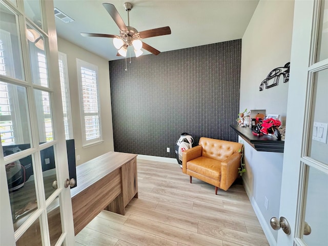 interior space with light wood finished floors, visible vents, an accent wall, baseboards, and wallpapered walls