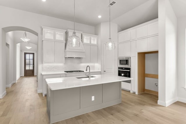 kitchen with a center island with sink, light countertops, glass insert cabinets, white cabinetry, and a sink