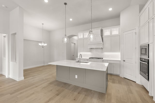 kitchen featuring arched walkways, glass insert cabinets, stainless steel appliances, light countertops, and a center island with sink