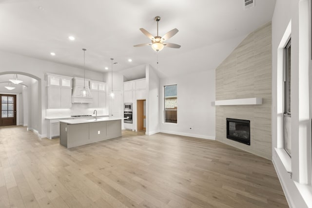 kitchen with a center island with sink, arched walkways, open floor plan, light countertops, and white cabinetry