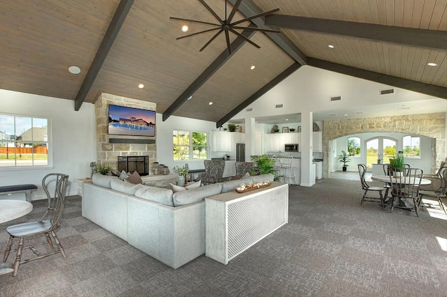 carpeted living room with arched walkways, wooden ceiling, a fireplace, high vaulted ceiling, and beam ceiling