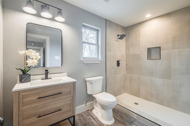 full bath with a tile shower, vanity, wood finished floors, and toilet