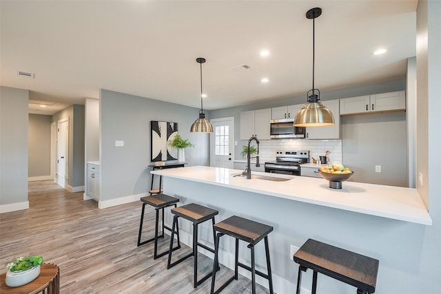 kitchen with light countertops, appliances with stainless steel finishes, a sink, and decorative light fixtures