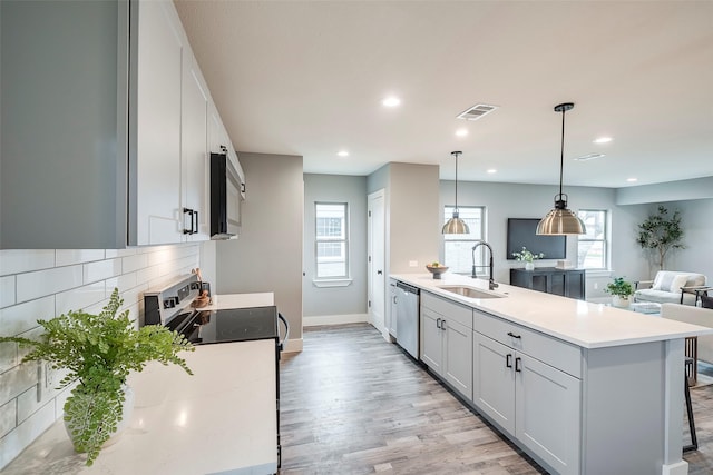 kitchen with a breakfast bar area, appliances with stainless steel finishes, decorative light fixtures, light countertops, and a sink