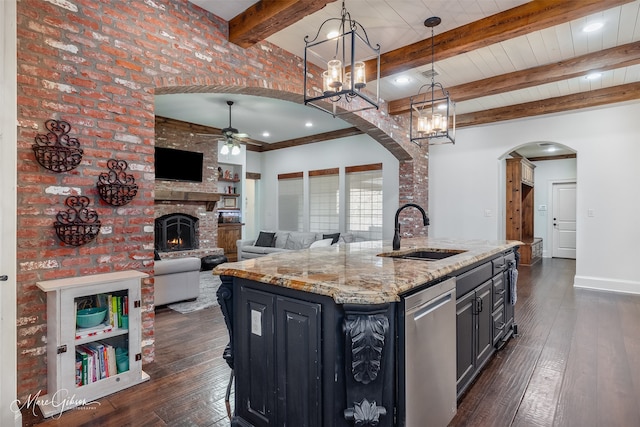 kitchen featuring a brick fireplace, dark wood-style floors, arched walkways, and a sink