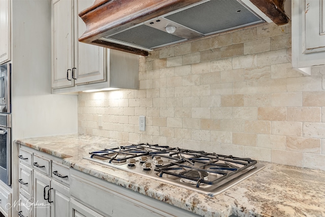 kitchen featuring light stone countertops, white cabinets, appliances with stainless steel finishes, under cabinet range hood, and tasteful backsplash