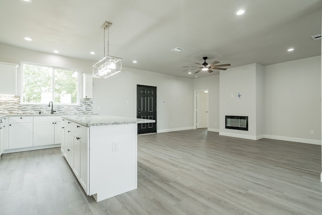 kitchen with white cabinets, a glass covered fireplace, light stone counters, open floor plan, and hanging light fixtures