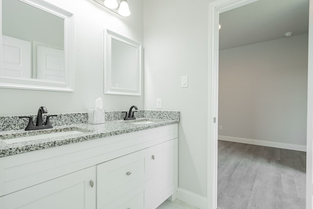 bathroom with double vanity, baseboards, a sink, and wood finished floors