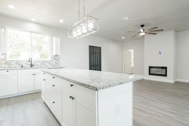 kitchen with visible vents, a kitchen island, white cabinetry, and pendant lighting