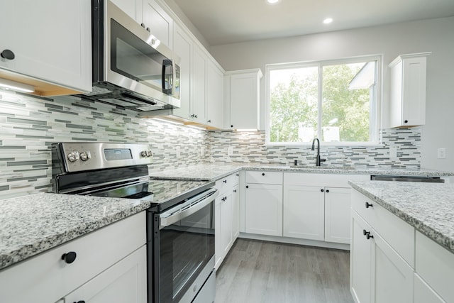 kitchen featuring decorative backsplash, appliances with stainless steel finishes, white cabinetry, a sink, and light stone countertops