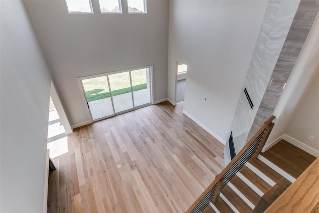 unfurnished living room with a towering ceiling, light wood-type flooring, and baseboards