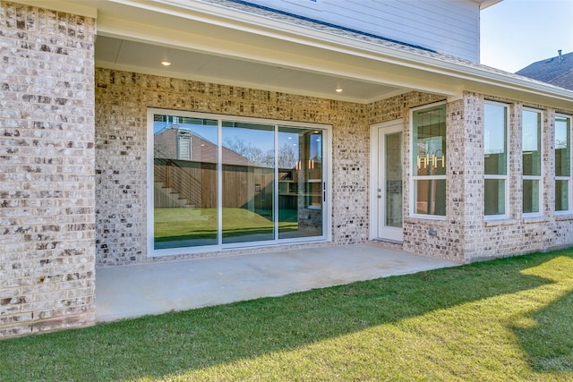 view of exterior entry with a patio, brick siding, and a lawn