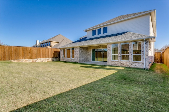 back of house with a fenced backyard, roof with shingles, a lawn, and brick siding