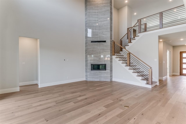 unfurnished living room featuring baseboards, a fireplace, a towering ceiling, and light wood-style floors