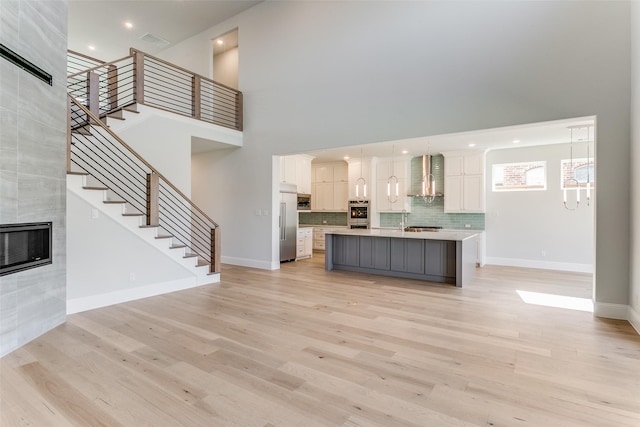 unfurnished living room featuring visible vents, light wood-style flooring, a tiled fireplace, and stairs