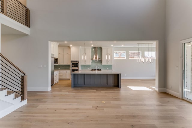 kitchen featuring pendant lighting, stainless steel appliances, light countertops, white cabinets, and an island with sink