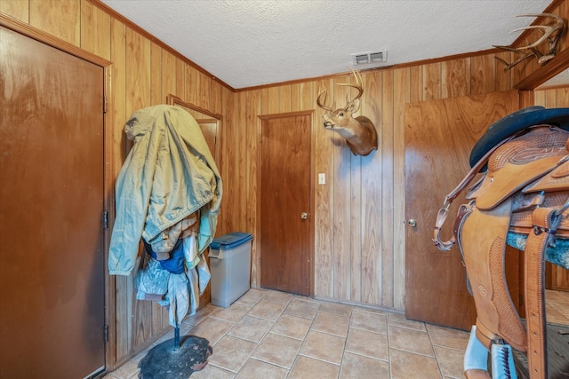 entryway featuring a textured ceiling, ornamental molding, wood walls, and visible vents