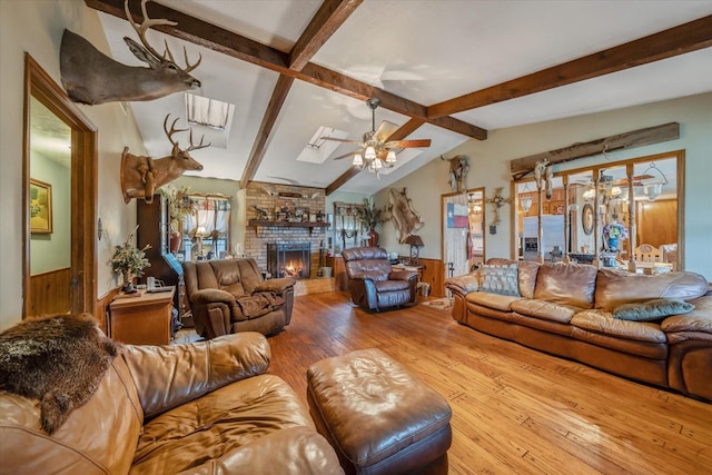 living area featuring a wainscoted wall, ceiling fan, lofted ceiling with skylight, light wood-type flooring, and a fireplace