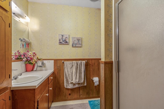 full bath featuring wallpapered walls, a stall shower, wainscoting, tile patterned flooring, and vanity