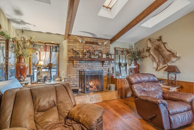 living area with light wood-style floors, lofted ceiling with skylight, wainscoting, and a brick fireplace