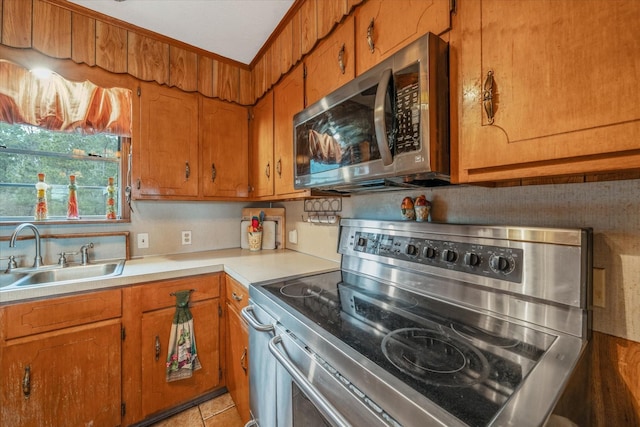 kitchen featuring brown cabinetry, appliances with stainless steel finishes, light countertops, and a sink