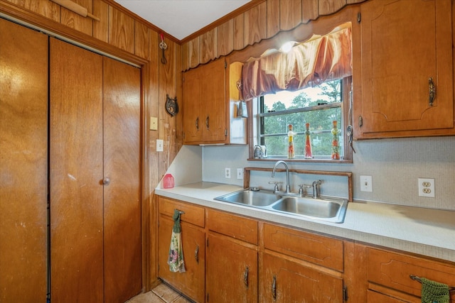 kitchen with brown cabinetry, light countertops, a sink, and crown molding