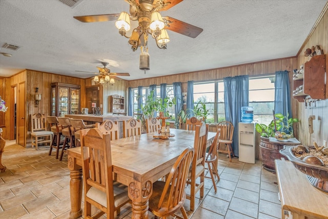 dining space featuring visible vents, wooden walls, and a textured ceiling