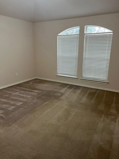 unfurnished room featuring dark colored carpet and baseboards