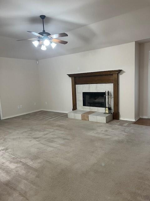 unfurnished living room with a tiled fireplace, carpet flooring, a ceiling fan, and baseboards