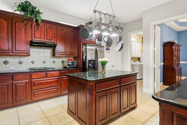 kitchen featuring under cabinet range hood, washing machine and clothes dryer, stainless steel fridge, and reddish brown cabinets