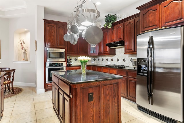 kitchen featuring under cabinet range hood, light tile patterned floors, decorative backsplash, arched walkways, and stainless steel appliances