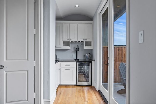 bar with lofted ceiling, beverage cooler, light wood-style flooring, and indoor wet bar