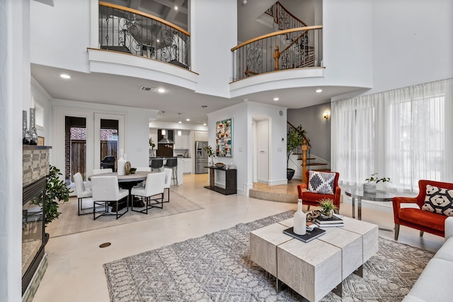 living area featuring a stone fireplace, recessed lighting, a towering ceiling, visible vents, and stairs