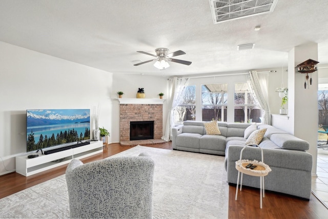 living area with visible vents, a ceiling fan, dark wood-style floors, a textured ceiling, and a fireplace