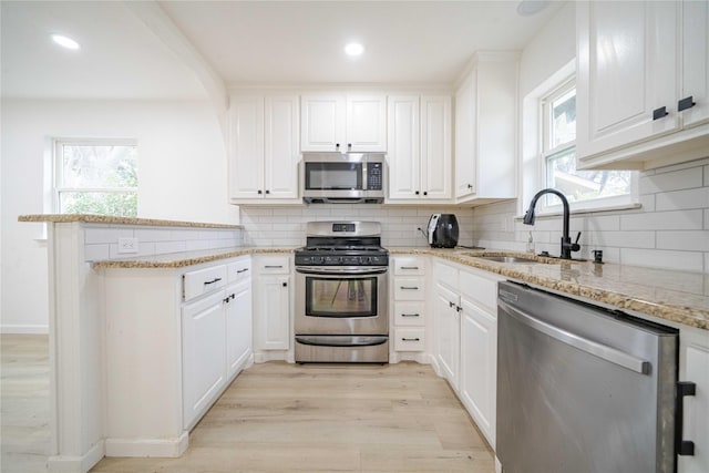 kitchen featuring appliances with stainless steel finishes, a sink, white cabinetry, and light wood-style floors