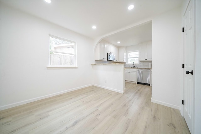 kitchen with light countertops, decorative backsplash, appliances with stainless steel finishes, white cabinetry, and a peninsula