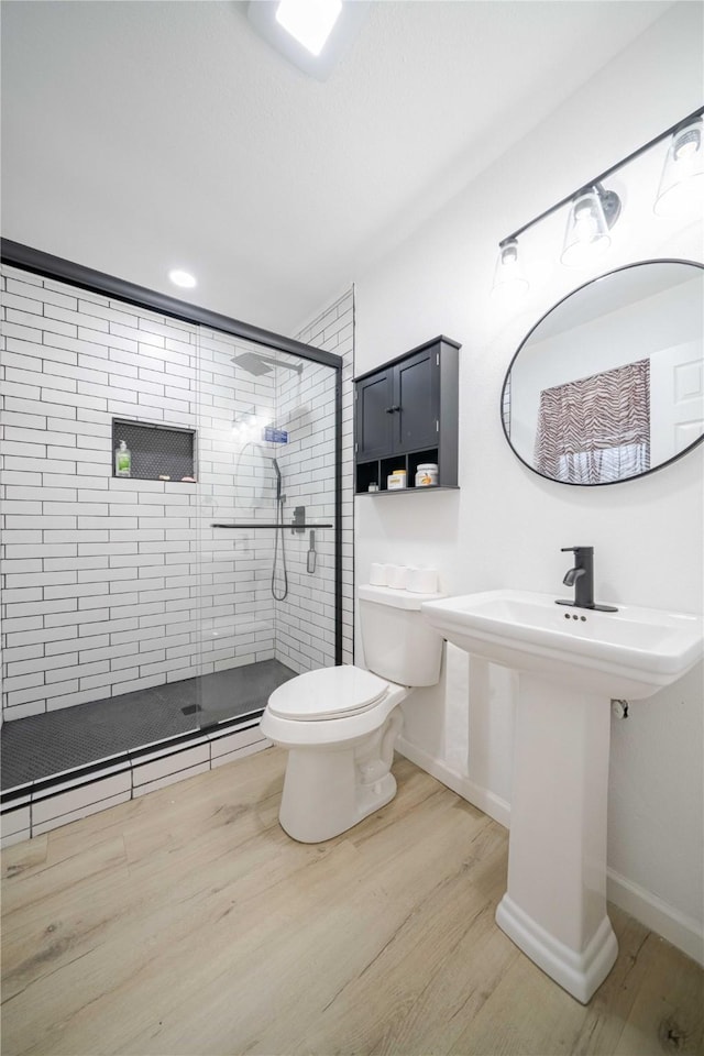 bathroom with a stall shower, wood finished floors, toilet, and baseboards