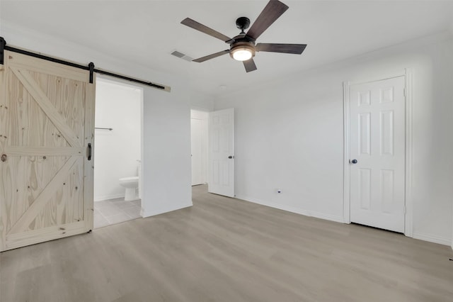 unfurnished bedroom with visible vents, light wood-style flooring, ensuite bath, and a barn door