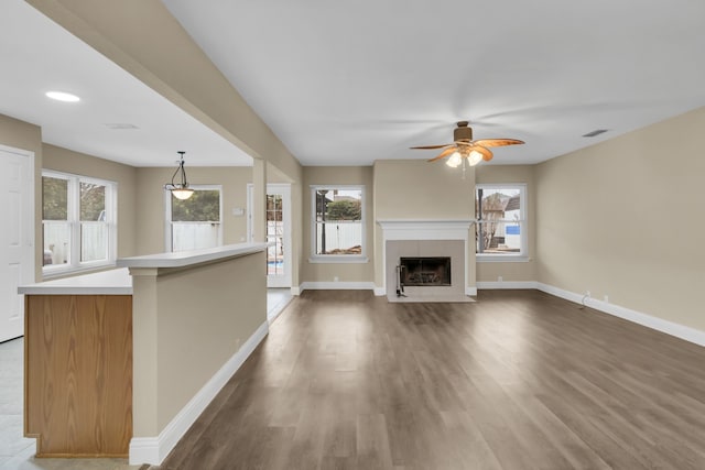unfurnished living room featuring wood finished floors, a tiled fireplace, a ceiling fan, and baseboards
