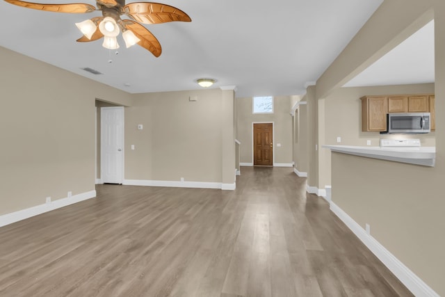unfurnished living room featuring light wood-style flooring, visible vents, a ceiling fan, and baseboards