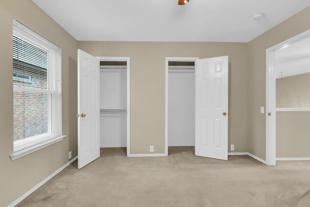 unfurnished bedroom featuring two closets, baseboards, and carpet