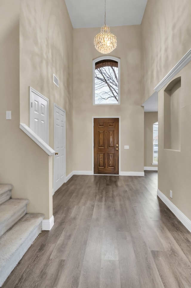 foyer entrance featuring wood finished floors, stairs, an inviting chandelier, a towering ceiling, and visible vents