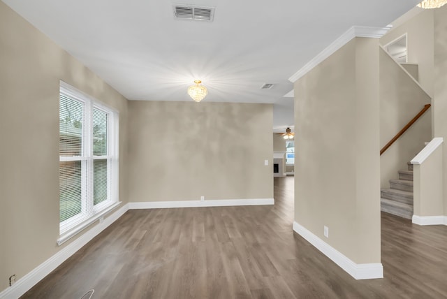 empty room with wood finished floors, visible vents, a ceiling fan, baseboards, and stairs