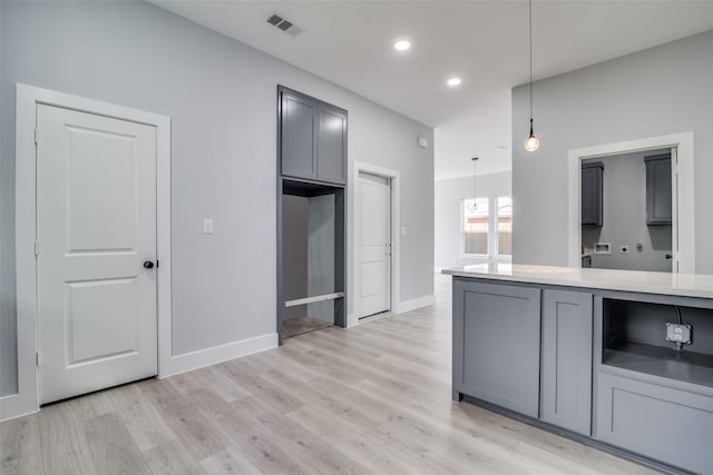 kitchen with decorative light fixtures, light wood finished floors, gray cabinets, visible vents, and light countertops